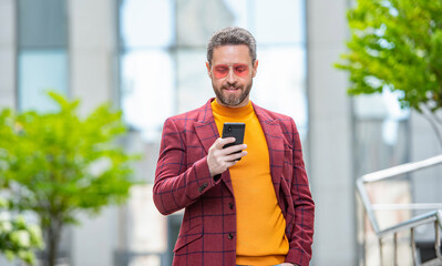 stylish man texting on smartphone outdoor. man texting on smartphone in the street.