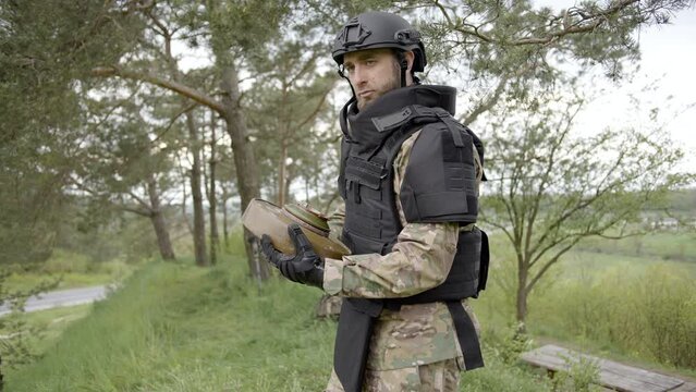 Demining. Male sapper carefully carries an anti-tank mine in his hands near the forest and looking forward