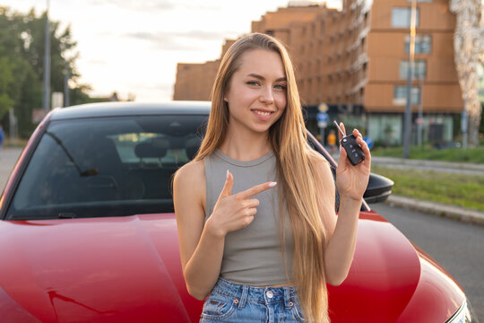 Young woman standing in front of her brand new car and shows on the key.