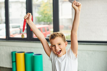 joyful preadolescent boy cheering and holding golden metal, smiling happily at camera, child sport