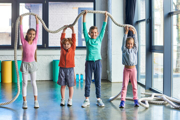 cheerful kids in sportswear raising fitness rope above heads and smiling at camera, child sport