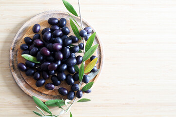 Olive nere in una ciotola e ramo di olive su fondo di legno. Cibo salutare. Vista dall'alto. Copia spazio. - obrazy, fototapety, plakaty