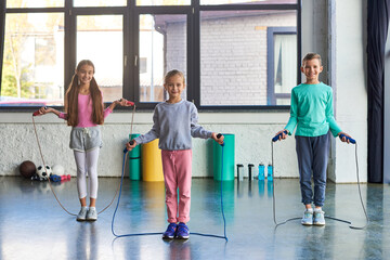 pretty little girls and boy smiling cheerfully at camera and holding skipping ropes, child sport