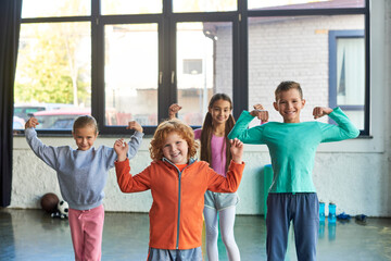 four pretty little children in sportswear playing muscles and smiling at camera, child sport - Powered by Adobe