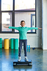 happy little cute boy standing on fitness stepper and smiling joyfully at camera, child sport