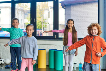 preadolescent cute boys and girls in sportswear stretching arms and smiling at camera, child sport