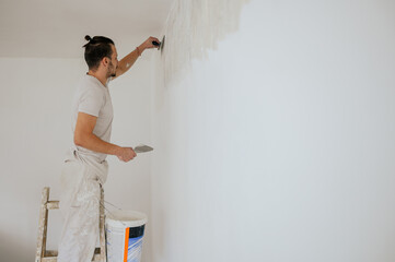 A plasterer on ladders is using tool and plaster for skim coating walls.