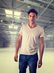 Trendy attractive young man standing in empty warehouse or industrial building, looking at camera