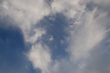 Aerial landscape on a summer day. High cirrus and low cumulus clouds hang in the light blue sky. They are at different levels and in different sizes. The blue sky is visible among the clouds.