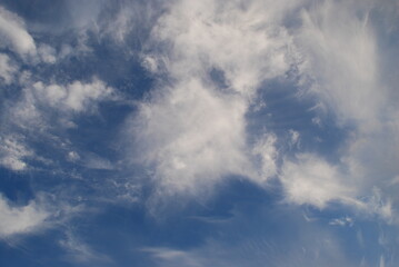 Aerial landscape on a summer day. High cirrus and low cumulus clouds hang in the light blue sky. They are at different levels and in different sizes. The blue sky is visible among the clouds.