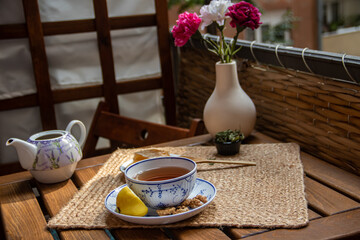 Morning setup on wooden table at balcony, books to read, cup of natural tea, teapot, organic honey from farm, fresh green tea leaves and organic fruits, in background nice view on small city park 
