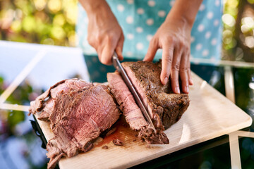 Cook cuts a juicy roast beef on a cutting board on a mirror table. Cropped