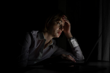 Side view of young tired businesswoman working on laptop at night. Work from home concept