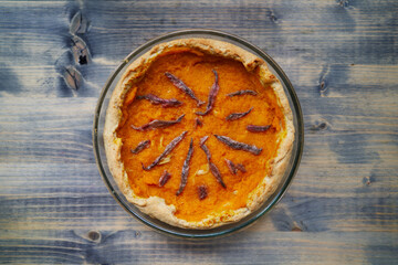 Pumpkin pie with anchovies in a glass dish stands on a wooden table. Top view - obrazy, fototapety, plakaty