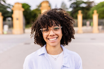 Portrait of young latin american girl with eyeglasses smiling at camera outdoors. Young positive...