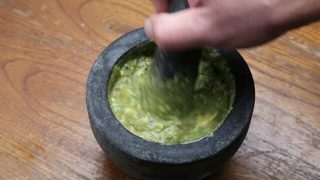 making guacamole (spicy mexican avocado dip served in a molcajete or stone mortar and pestle) cilantro, onion, tomato, jalapeno pepper (man's hand, caucasian model)