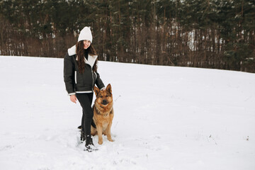 Young woman walk the dog German Shepherd in winter field forest, running playing with snow, training the animal in harsh conditions, wind blowing. Christmas Time, New Year