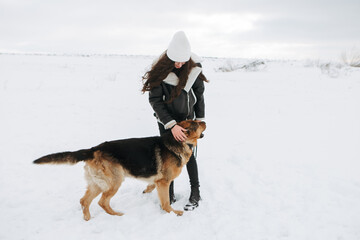 Young woman walk the dog German Shepherd in winter field forest, running playing with snow, training the animal in harsh conditions, wind blowing. Christmas Time, New Year