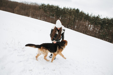 Young woman walk the dog German Shepherd in winter field forest, running playing with snow, training the animal in harsh conditions, wind blowing. Christmas Time, New Year