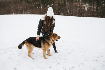 Young woman walk the dog German Shepherd in winter field forest, running playing with snow, training the animal in harsh conditions, wind blowing. Christmas Time, New Year
