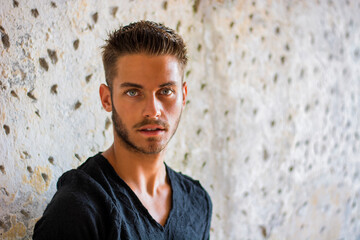 Fototapeta premium A man standing in front of a stone wall. Photo of a man posing in front of a textured stone wall