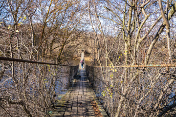 People walk along an old wooden canopy bridge across the river.