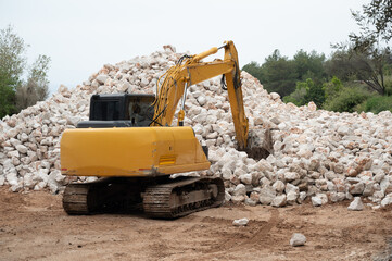 Yellow excavator standing near pile of stones