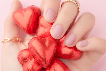 Womans hand with trendy pink matte manicure holding candy close-up