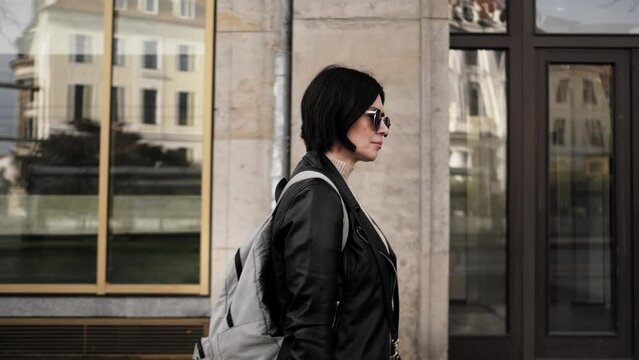Attractive Woman In Sunglasses Walks Down City Street With Backpack