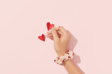 Beautiful well-groomed female hand with pink matte nails holding paper heart on a pink background....