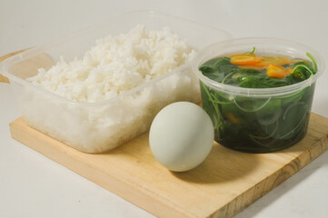a menu of white rice with clear vegetables of spinach leaves and carrots and a salted egg on a wooden board isolated on a white background