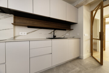 Newly installed kitchen with white handleless cabinets, integrated appliances with black resin...