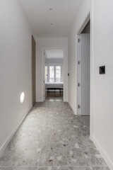 Distributor hallway of a modern home with gray terrazzo floors, plain white painted walls and a light integrated into the wall