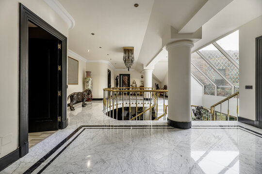 Entrance halls and staircase area of a luxury townhouse with polished marble floors, golden metal railings and skylight with terrace