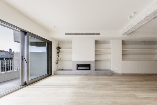Front image of the living room of a recently renovated modern home with built-in furniture on one side, gray fireplace, wooden floors and terrace with views of the neighbors