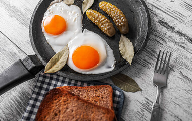 Fried eggs in a frying pan with pickled cucumbers.