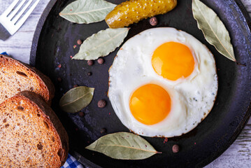 Fried eggs in a frying pan with pickled cucumbers.