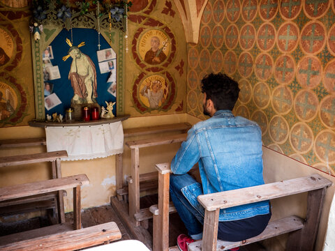 A man sitting on a bench in a church. Photo of a man sitting on a bench inside a beautiful small chapel