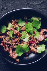 Spicy carpaccio salad with green coriander, lime, sesame seeds and red hot chili pepper in a black...