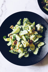 Healthy salad with fresh vegetables - cucumber, avocado, walnuts, feta cheese and coriander on a bowl.