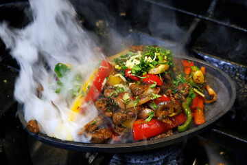 mexican food smoking chicken and beef fajitas on hot sizzling plate with fire and smoke