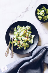 Healthy salad with fresh vegetables - cucumber, avocado, walnuts, feta cheese and coriander on a bowl.