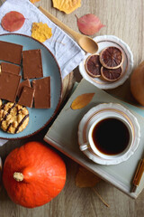 Cup of tea or coffee, plate with cookies and chocolate, dried oranges, bowl of grapes, vintage books, pumpkins and autumn leaves on the table. Autumnal hygge. Top view.