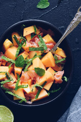Healthy salad with salmon, melon, mint and lime in a black bowl