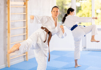 Two female karateka focused intently on perfecting their roundhouse kicks during training.