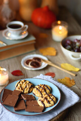 Cup of tea or coffee, plate with desserts, dried oranges, bowl of grapes, scented candles, vintage books, pumpkins and autumn leaves on the table. Autumnal hygge. Selective focus.
