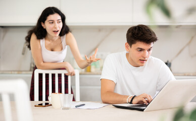 Young woman screams during family quarrel with young guy using laptop in kitchen