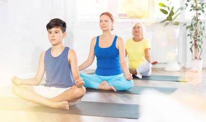 Tuinposter Mother, grandmother and adolescence son do exercise half lotus position of Ardha Padmasana Sidhasana with hands clasped in mudra knowledge pose. Concept of communication of generations, joint leisure © JackF