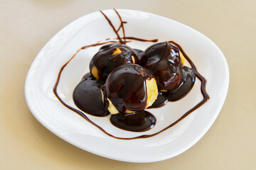 Delicious profiteroles with chocolate and plate. Selective focus image on light background.