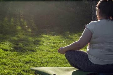 Poster Portrait of overweight Caucasian middle-aged woman practicing yoga in nature. Fat woman meditating, relaxing in lotus position, sitting on fitness mat. Calm, relaxed, zen, stop stress. View from back © lilu2005